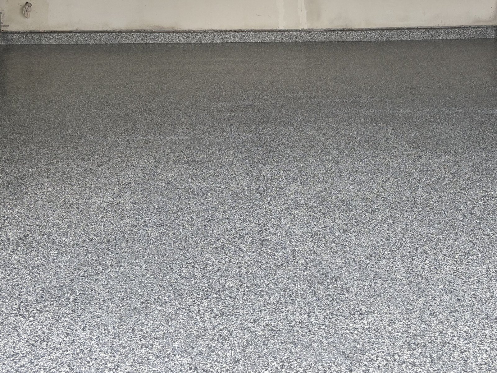 Finished two-car garage floor in grey and black flake, the coating carried up the wall as a coved base.