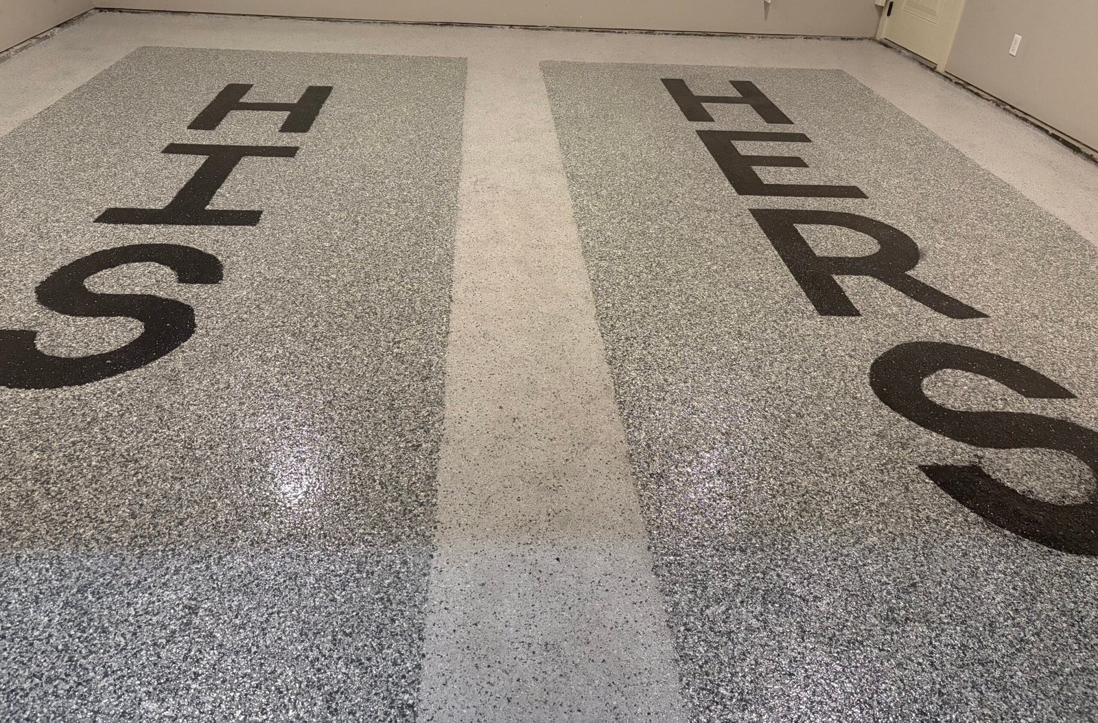 Two-bay garage floor in grey flake, with HIS and HERS set into the coating in dark flake and a pale aisle strip running between the bays.